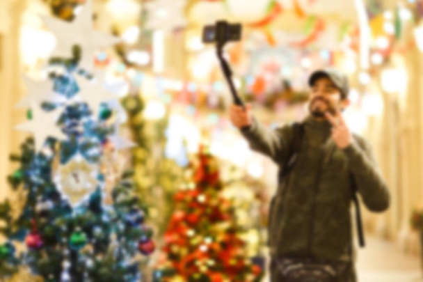 Рождественская ель в магазине, на размытом фоне человека, делающего селфи
. - Фото, изображение