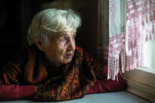 Elderly woman looks longingly out the window. - Photo, Image