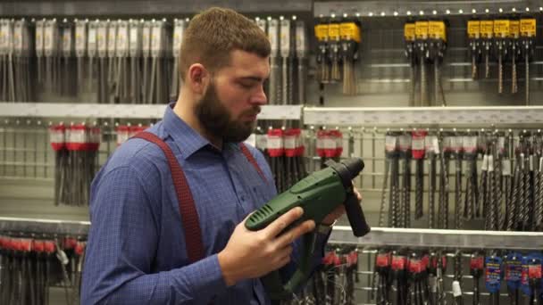 Een man in een ijzerhandel kiest een elektrische hamer boor. - Video