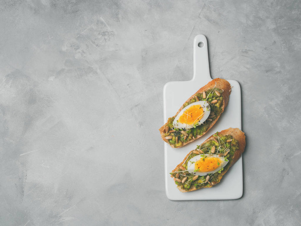 Fresh whole-grain toasts plated avocado with eggs, fresh mini herbs, sunflower seeds and sprinkled black salt served on ceramic white board - Foto, imagen