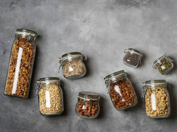 Pile of almond, cashew, peanuts, hazelnuts, walnuts and Chia seeds, sunflower and pumpkin seeds in glass jars on concrete background - Foto, Imagen