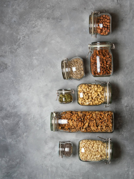 Row of almond, cashew, peanuts, hazelnuts, walnuts and Chia seeds, sunflower and pumpkin seeds in glass jars on concrete background - Foto, Imagen