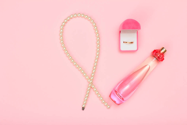Korálky, lahvičku parfému a Zlatý kroužek v poli na růžovém pozadí. Ženy kosmetika a doplňky. Pohled shora. - Fotografie, Obrázek