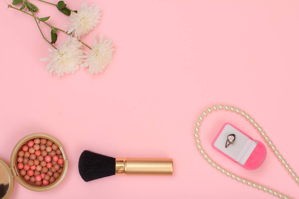 Box mit Ring, Perlen, Puder, Pinsel und Blumen auf rosa Hintergrund. Kosmetik und Accessoires für Frauen. Ansicht von oben mit Kopierraum. - Foto, Bild