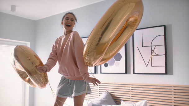 Nainen, jolla on kultaisia ilmapalloja juhlii syntymäpäiväänsä sängyssä
 - Materiaali, video
