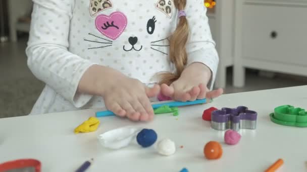 uma menina brinca com plasticina, bolas de rolos, há figuras e lápis coloridos na área de trabalho, o desenvolvimento de habilidades motoras finas de mãos
 - Filmagem, Vídeo