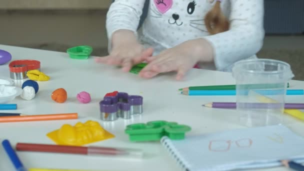 ένα μικρό κορίτσι παίζει με πλαστελίνη, ρολά μπάλες, υπάρχουν στοιχεία και χρωματιστά μολύβια στην επιφάνεια εργασίας, την ανάπτυξη της λεπτές κινητικές δεξιότητες των χεριών - Πλάνα, βίντεο