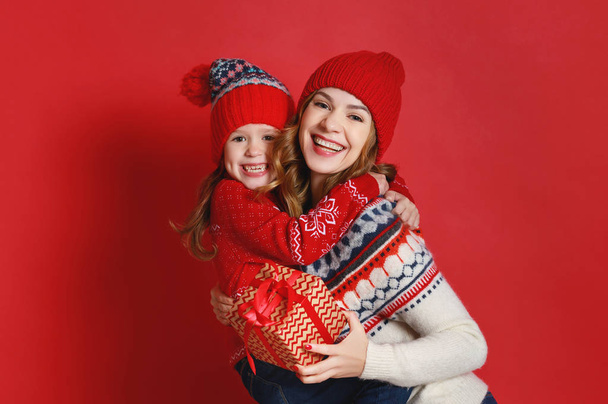 gelukkige familie moeder en kind dochter met Kerstcadeaus en hoeden op rode achtergrond - Foto, afbeelding
