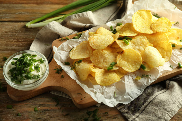 Ízletes burgonya chips, tejföllel és gyógynövényekkel, fából készült háttér - Fotó, kép