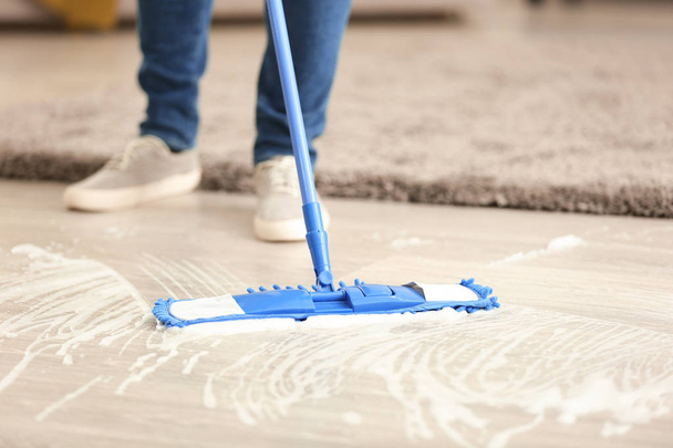 Nuori mies puhdistaa lattiaa asunnossaan
 - Valokuva, kuva