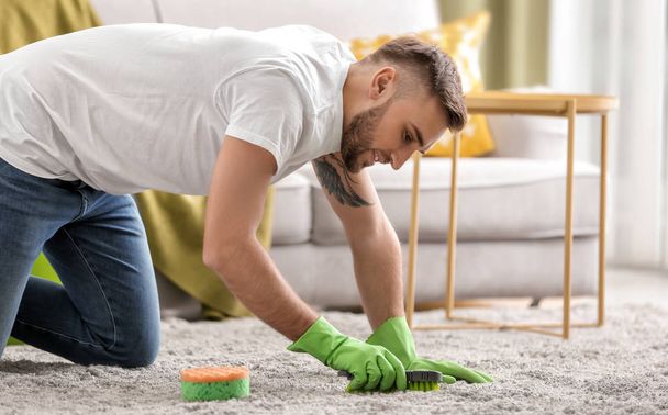 Young man cleaning carpet at home - Фото, изображение