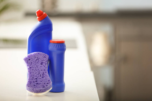 Бутылки с моющими средствами и губкой на столе на кухне
 - Фото, изображение