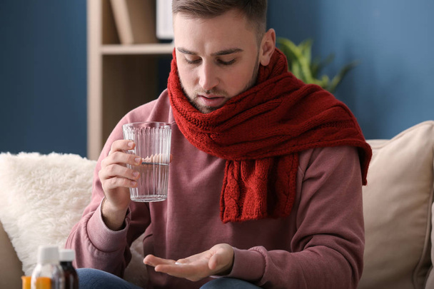 Young man ill with flu taking medicine at home - Foto, afbeelding