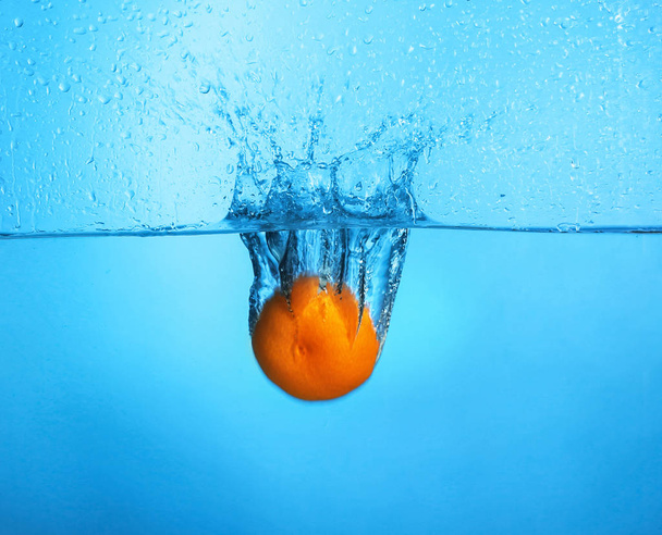 Падение мандарина в воду на цветном фоне
 - Фото, изображение