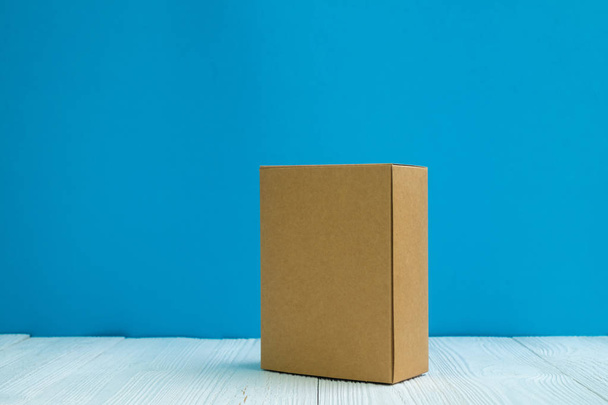 Empty Package brown cardboard box or tray on bright white wooden table with blue wall background. copy space for add text or advertising word. - Foto, Imagem