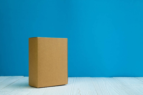 Empty Package brown cardboard box or tray on bright white wooden table with blue wall background. copy space for add text or advertising word. - Photo, Image