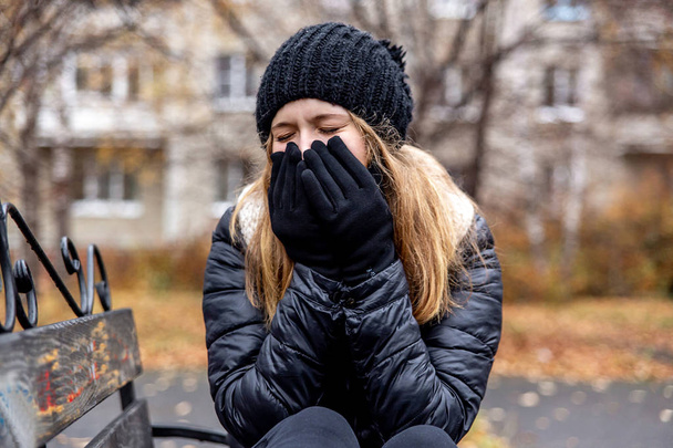 a young sick woman is sneezing outside - Foto, Bild