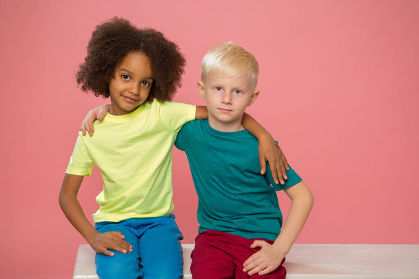 Seitenansicht von kleinen Kindern. Glückliches Paar von Kindern isoliert auf rosa Hintergrund. Afroamerikanische und weiße Kinder zusammen. Schwarze Leben, Kindheit, Freundschaftskonzept. - Foto, Bild