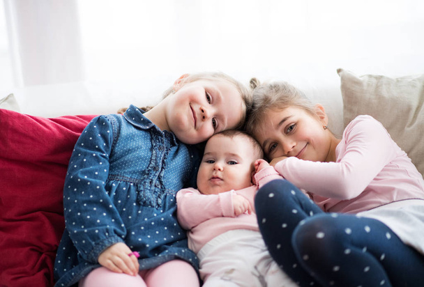 A portrait of three small girls sitting indoors on a sofa. - Foto, Imagen