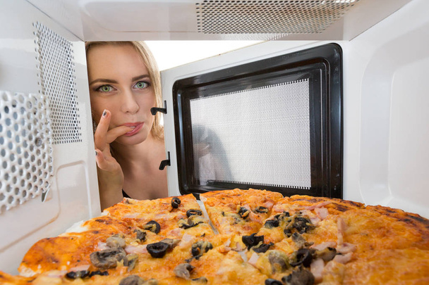 Girl looking at a pizza in the microwave - Foto, afbeelding