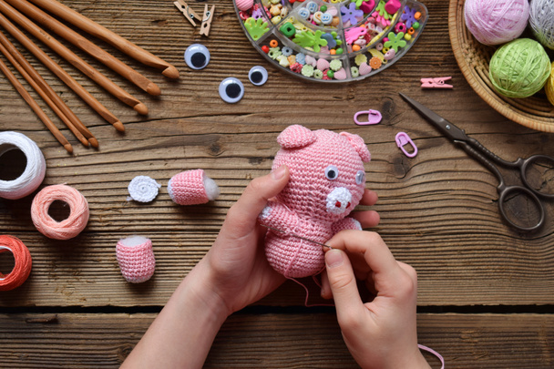 ピンクのブタを作る。かぎ針編みの子供のためのおもちゃ。表スレッド、針、フック、綿の糸。ステップ 2 - グッズのすべての詳細を縫う。手作りの工芸品。Diy のコンセプトです。中小企業です。趣味からの収入. - 写真・画像