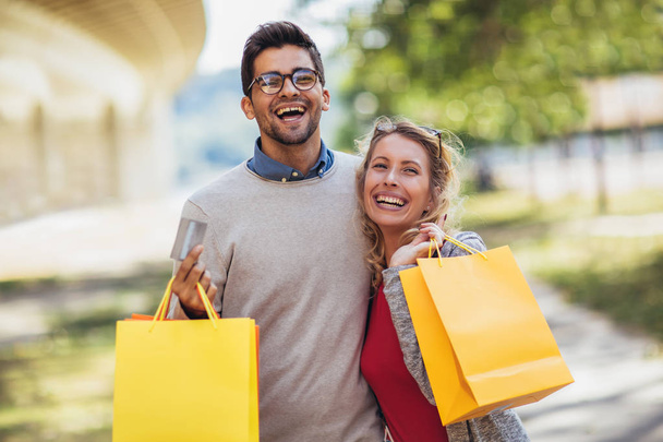 Portrét šťastnému páru s nákupní tašky po nakupování v městě usmívá a držení platební karty - Fotografie, Obrázek