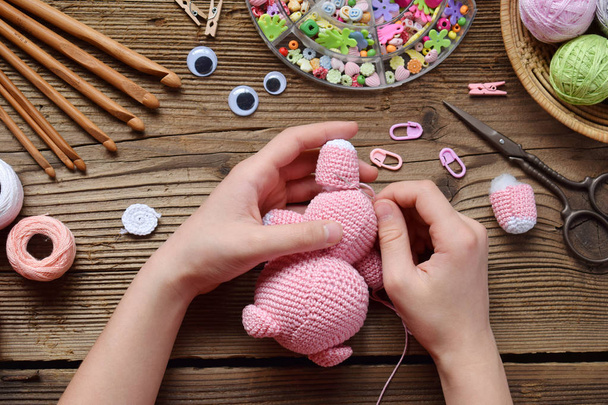 Making pink pig. Crochet toy for child. On table threads, needles, hook, cotton yarn. Step 2 - to sew all details of toy. Handmade crafts. DIY concept. Small business. Income from hobby. - Photo, Image