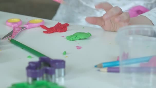 uma menina brinca com a plasticina, esculpe uma figura, há figuras e lápis coloridos na área de trabalho, o desenvolvimento de habilidades motoras finas de mãos
 - Filmagem, Vídeo