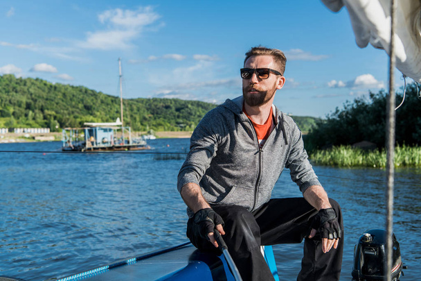 Egy ember visel, napszemüveget és alkalmi ruhák, vezet egy kis csónak körül egy tó vagy folyó - Fotó, kép