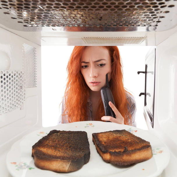 Girl looking to a burned toasts in microwave - Foto, Bild