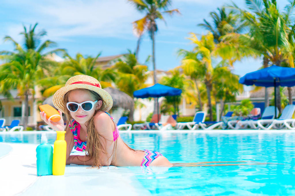 Menina com garrafa de creme solar na piscina
 - Foto, Imagem