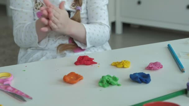 Szczęśliwa dziewczynka bawi się kolorowe plasteliny, rzeźbi postać, na pulpicie są dane liczbowe i kredki, rozwoju zdolności motoryczne rąk - Materiał filmowy, wideo