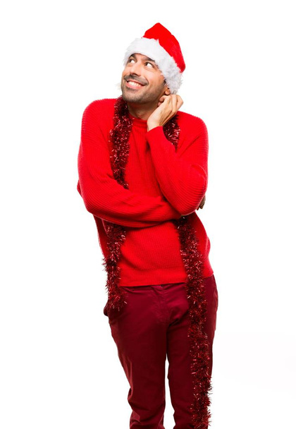 Homem com roupas vermelhas comemorando as férias de Natal de pé e pensando em uma ideia enquanto coça a cabeça no fundo branco isolado
 - Foto, Imagem