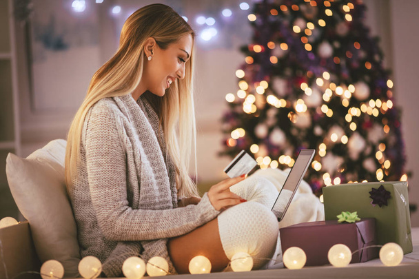 Happy young woman relaxing at home and buying online Christmas presents on laptop - Foto, afbeelding