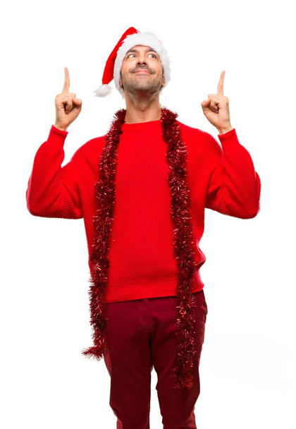Άνθρωπος με κόκκινα ρούχα, γιορτάζουμε τις διακοπές των Χριστουγέννων δείχνοντας με το δάχτυλο δεικτών μια μεγάλη ιδέα σε απομονωμένες άσπρο φόντο - Φωτογραφία, εικόνα