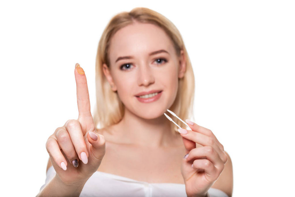 Focus on contact lens on finger of young woman. Young woman holding contact lens on finger in front of her face. Woman holding contact lens on white background. - Photo, Image