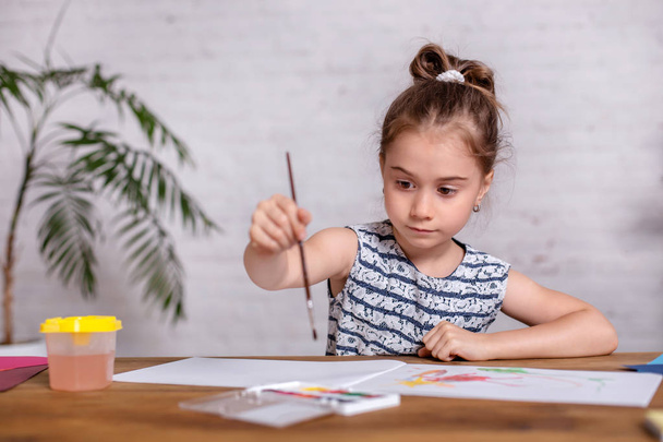 Petite fille inspirée à la table dessiner avec des peintures
 - Photo, image
