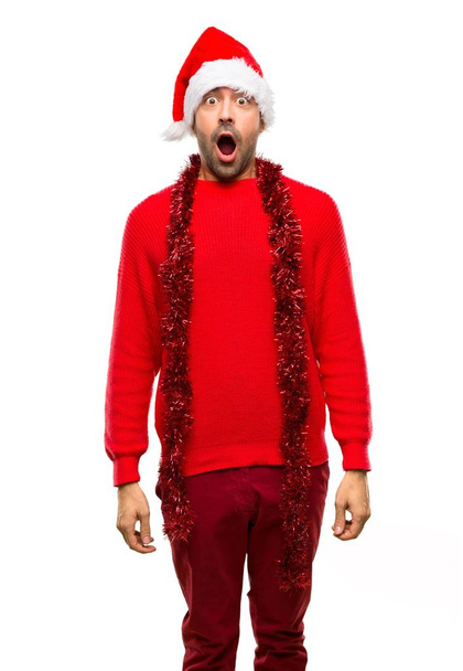 Uomo con abiti rossi che celebrano le vacanze di Natale con sorpresa e espressione facciale scioccata su sfondo bianco isolato
 - Foto, immagini