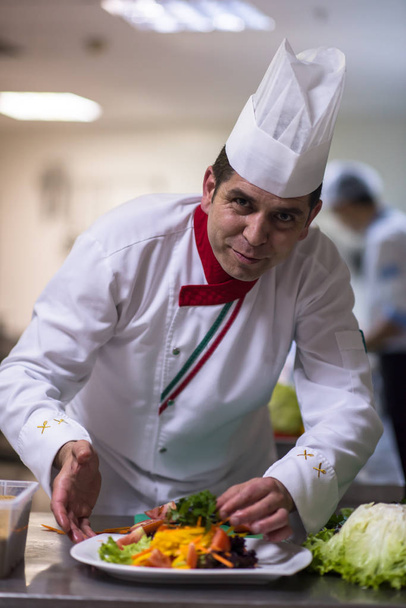 chef que sirve ensalada de verduras en el plato en la cocina del restaurante - Foto, Imagen
