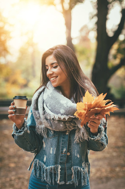 Nuori nainen kävelee ja juo kahvia syksyllä puistossa
 - Valokuva, kuva