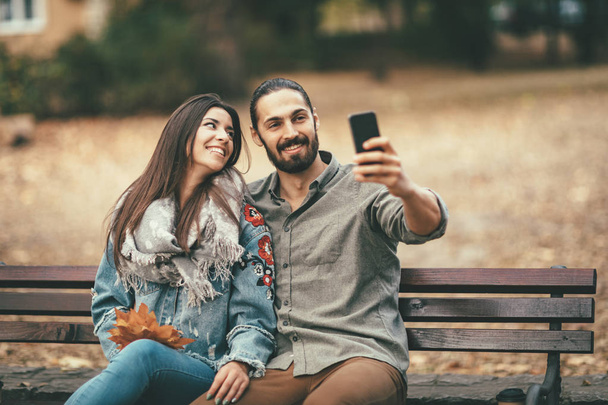 smiling couple sitting on bench and using smartphone - Foto, Imagen
