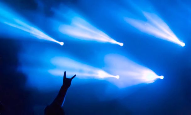 Mano mostrando letrero de rock heavy metal, una señal de los cuernos, con luces de escenario azules en el fondo durante el festival Metalshow al aire libre en Letonia
. - Foto, imagen