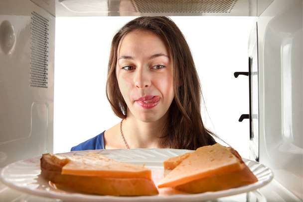 Girl lickoing to the sandwich. Through microwave oven view - Foto, afbeelding