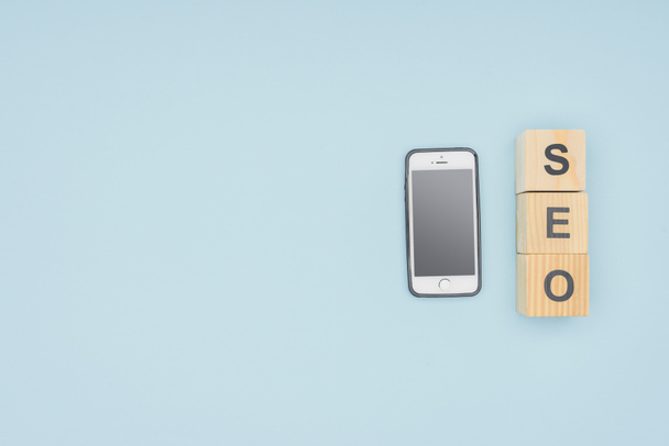 Плоский прошарок смартфона біля кубиків з буквами ізольовані на світло-блакитному
  - Фото, зображення