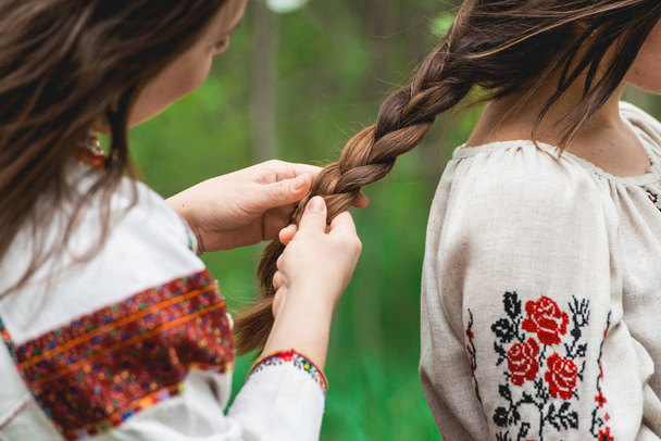 Conceito de lazer feminino. Irmãs, melhores amigos em roupas tradicionais ucranianas fazendo trança, penteado uns aos outros
 - Foto, Imagem