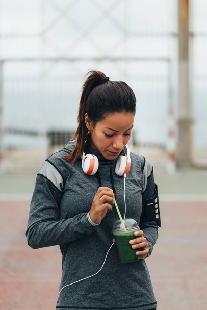 Jovem mulher fitness bebendo desintoxicação smoothie verde durante o descanso treino da cidade ao ar livre. Nutrição desportiva e conceito de estilo de vida saudável
. - Foto, Imagem