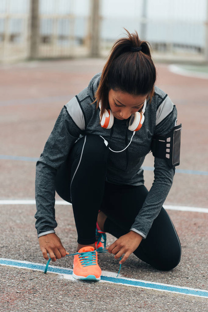 Woman lacing sport footwear before running or exercising. Outdoor city workout concept. Female fitness athlete getting ready for working out. - Photo, Image