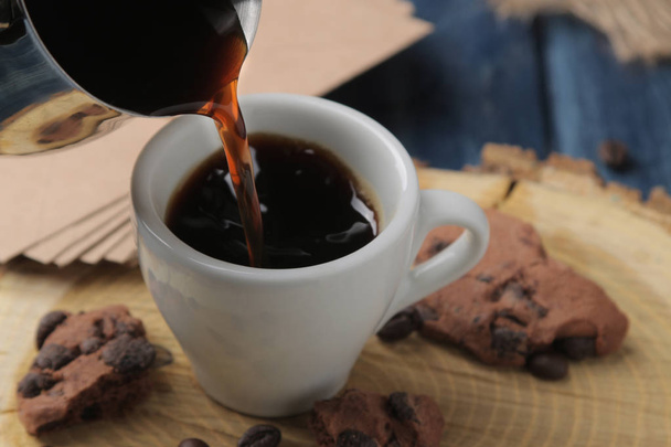 Природный кофе эспрессо наливают с Cezve в чашку на синем деревянном столе
 - Фото, изображение