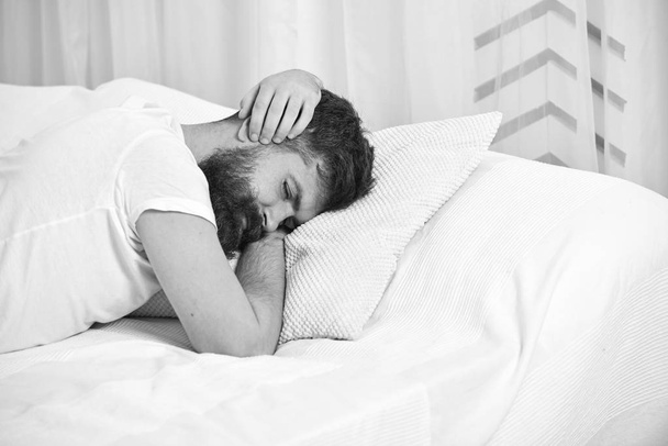 Man in shirt laying on bed covering ears with hands, white curtain on background. Wake up call concept. Macho with beard and mustache refuses to get up. Guy on sleepy tired face keep sleeping - Foto, Bild