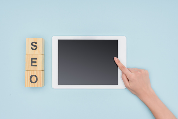 Top view of female seo manager pointing at digital tablet near wooden cubes  on light blue background  - Photo, Image